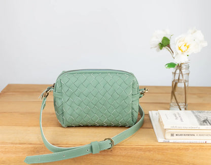 Green woven handbag on a wooden surface with a white background