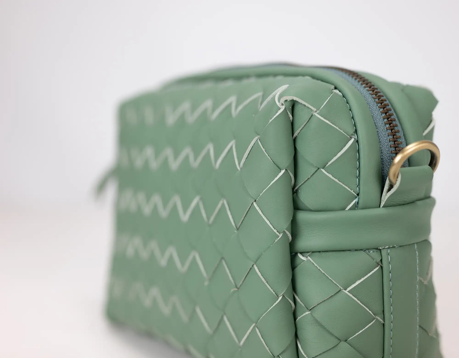 Green woven handbag with a gold zipper on a white background