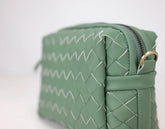 Green woven handbag with a gold zipper on a white background