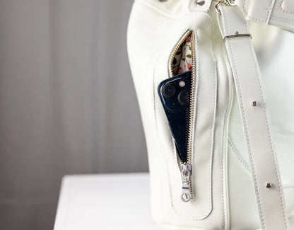 White leather handbag with a phone inside a pocket on a neutral background