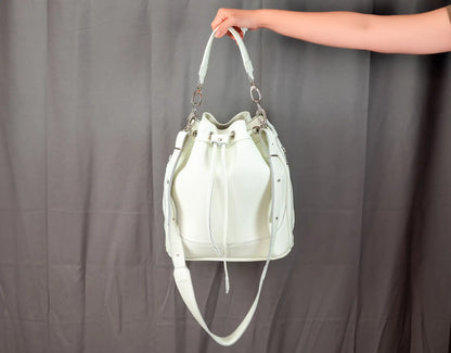 White leather handbag held by a person against a gray background