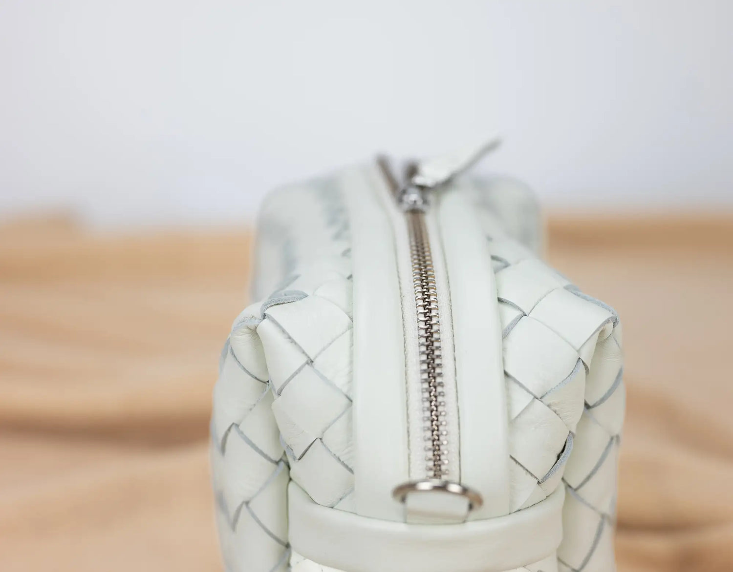 White woven handbag with a silver zipper on a wooden surface