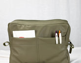 Green bag with pockets containing stationery items on a white background