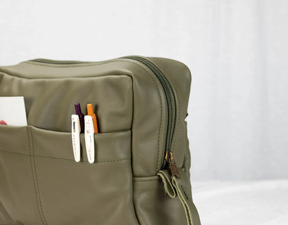 Green bag with a pocket containing colorful markers on a white background