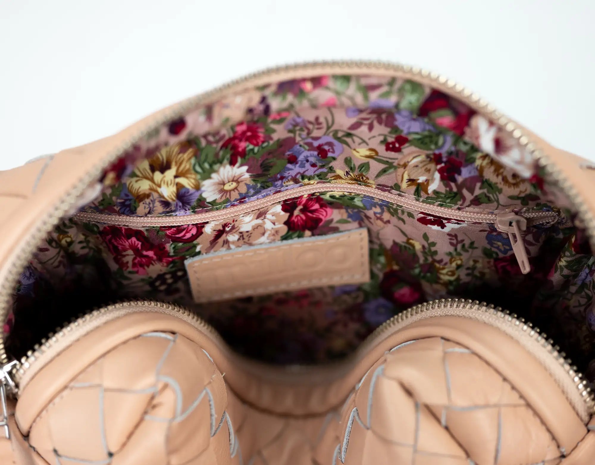 Close-up of a beige handbag with floral interior on a light gray background