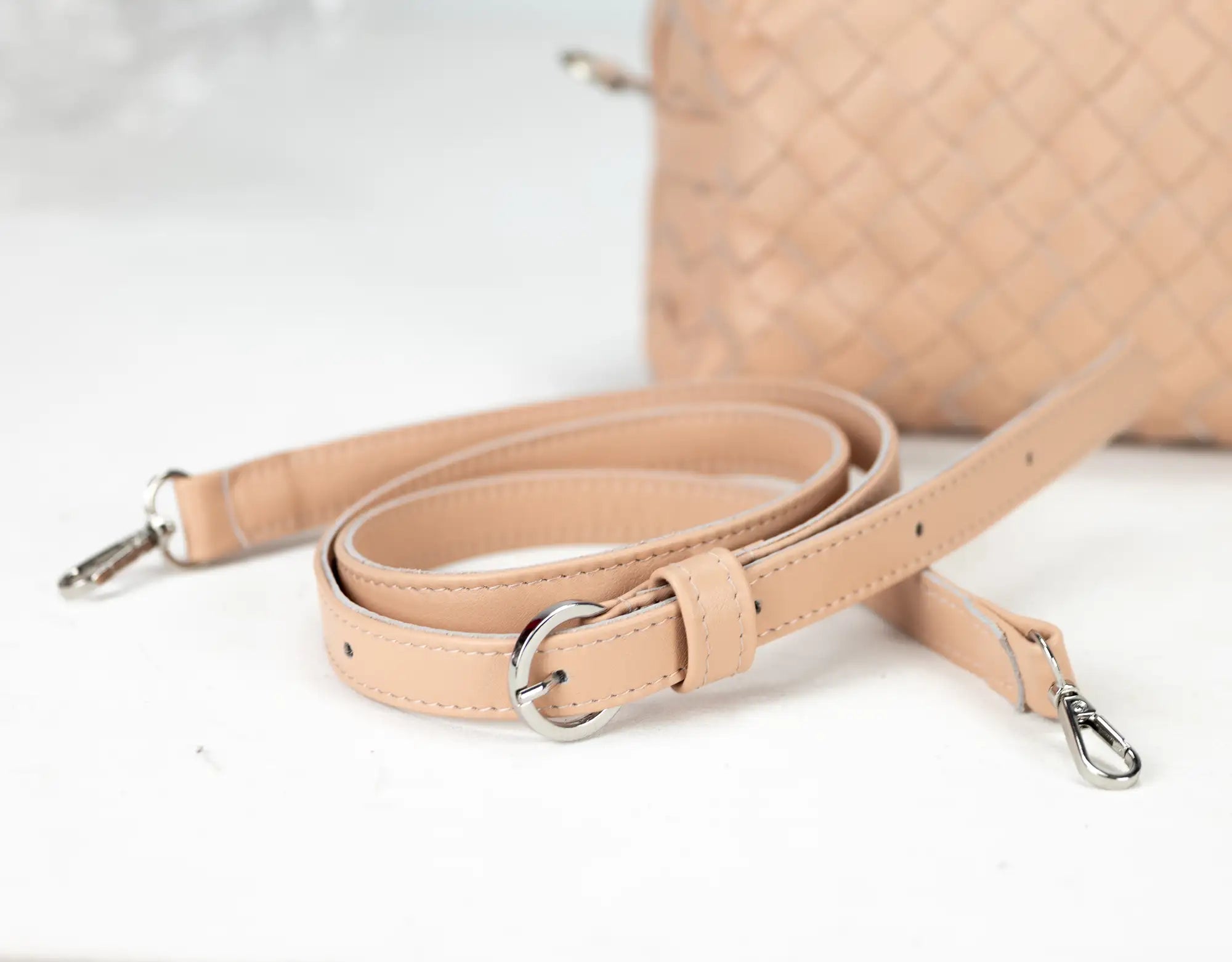 Beige leather bag strap with metal hardware on a light background