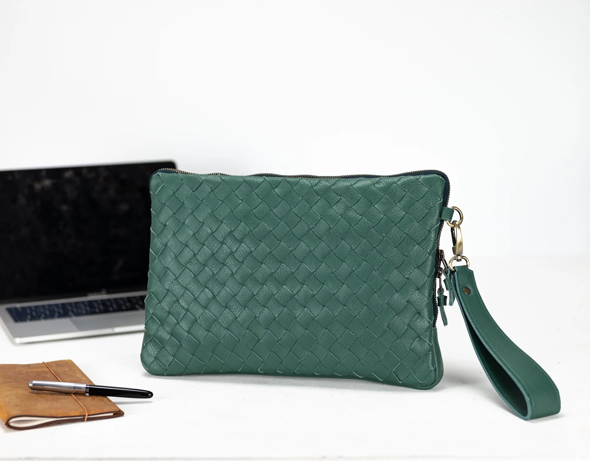 Green woven clutch bag with a laptop and notebook on a white background