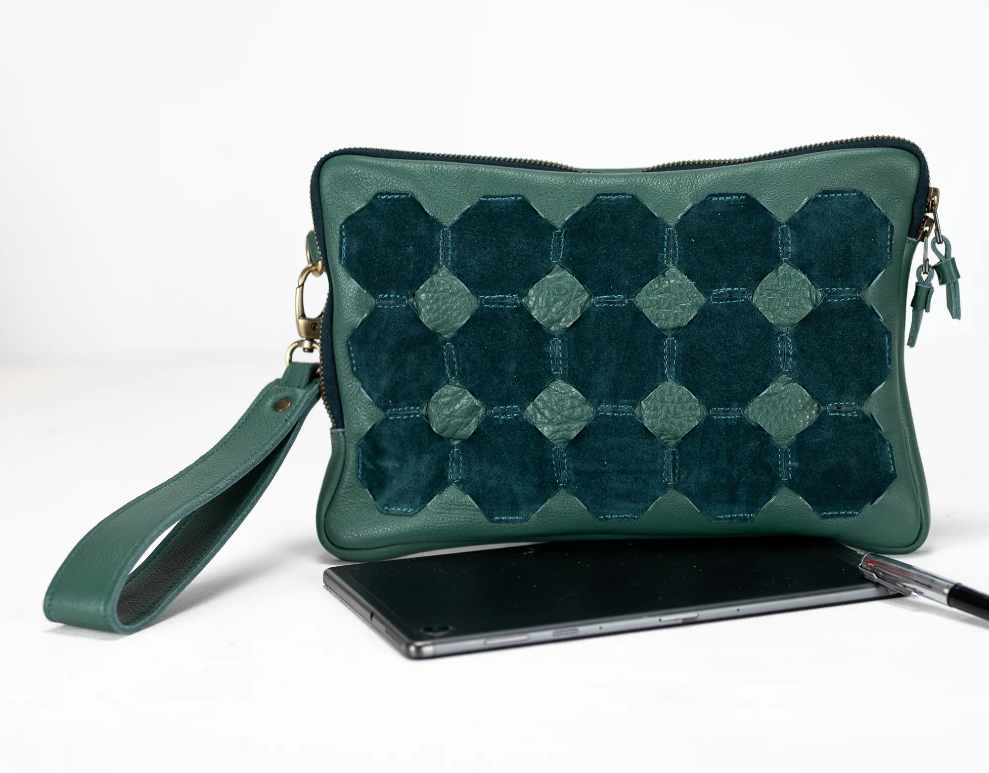 Green quilted clutch bag with a phone and pen on a white background