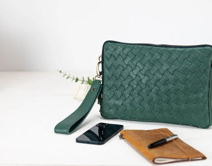 Green woven clutch bag with phone and notebook on a white background