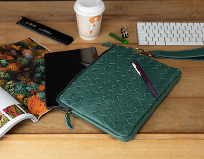 Green woven clutch on a wooden surface with a magazine, coffee cup, and keyboard in the background.