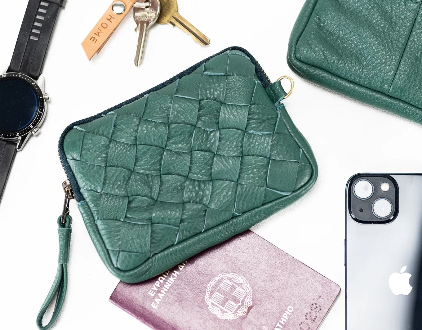 Green leather pouches with a phone, keys, watch, and passport on a white background