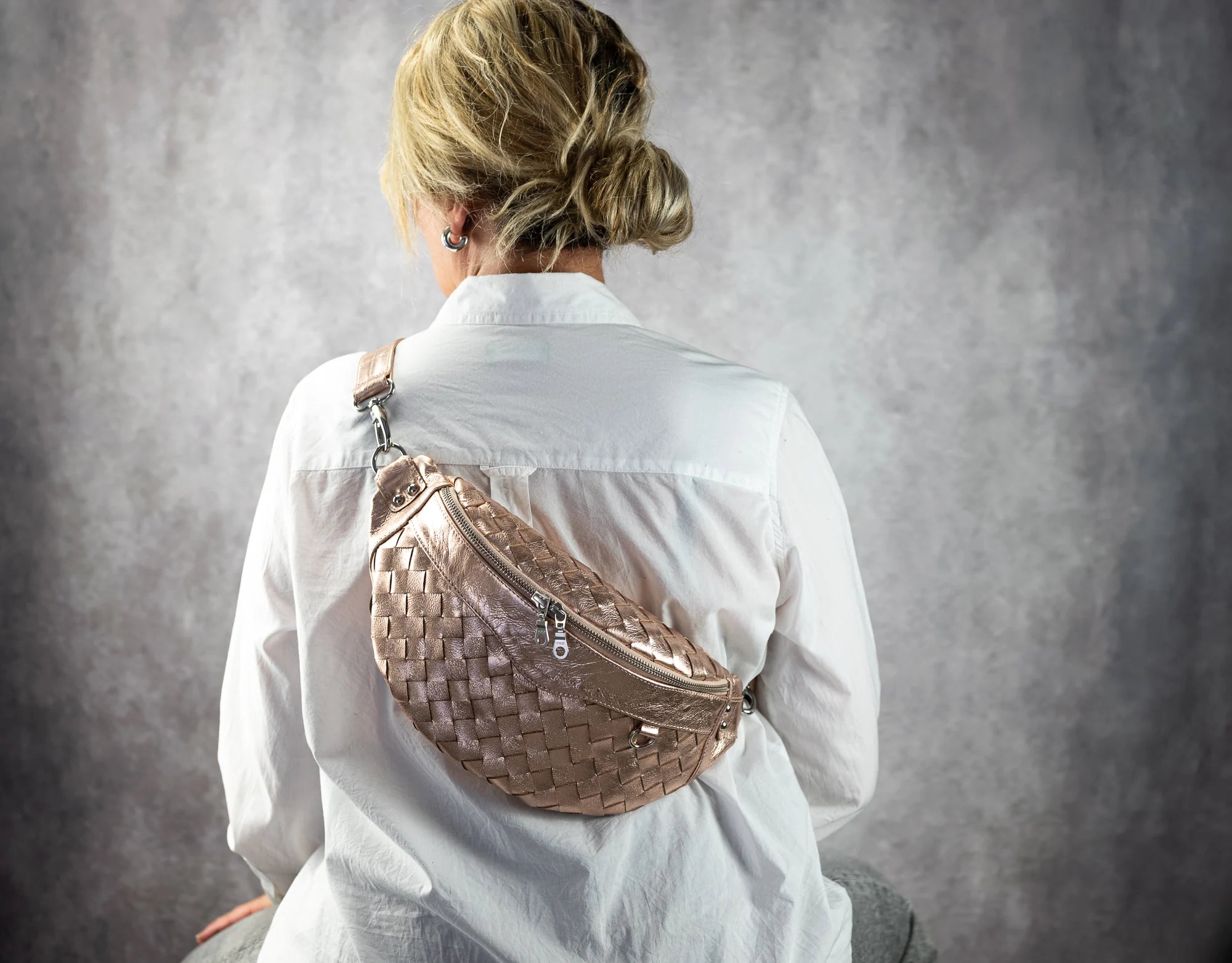 Person wearing a woven rose gold backpack on a plain background