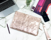 Rose gold clutch on a marble surface with laptop, phone, and glasses.