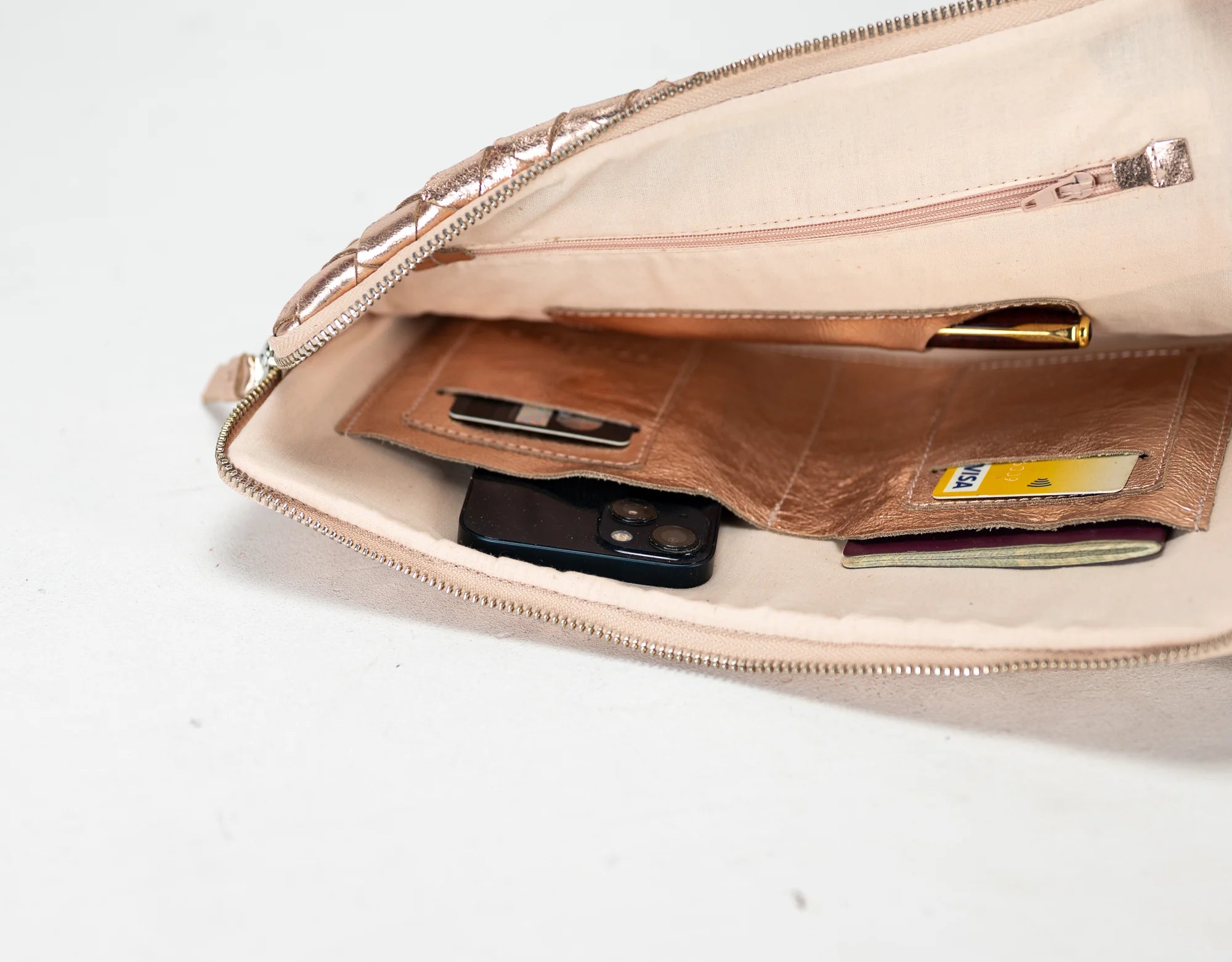 Beige clutch bag with a brown wallet and phone inside on a white background