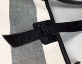 Close-up detail of a black pebbled leather strap crossing over a white and gray striped textile surface.