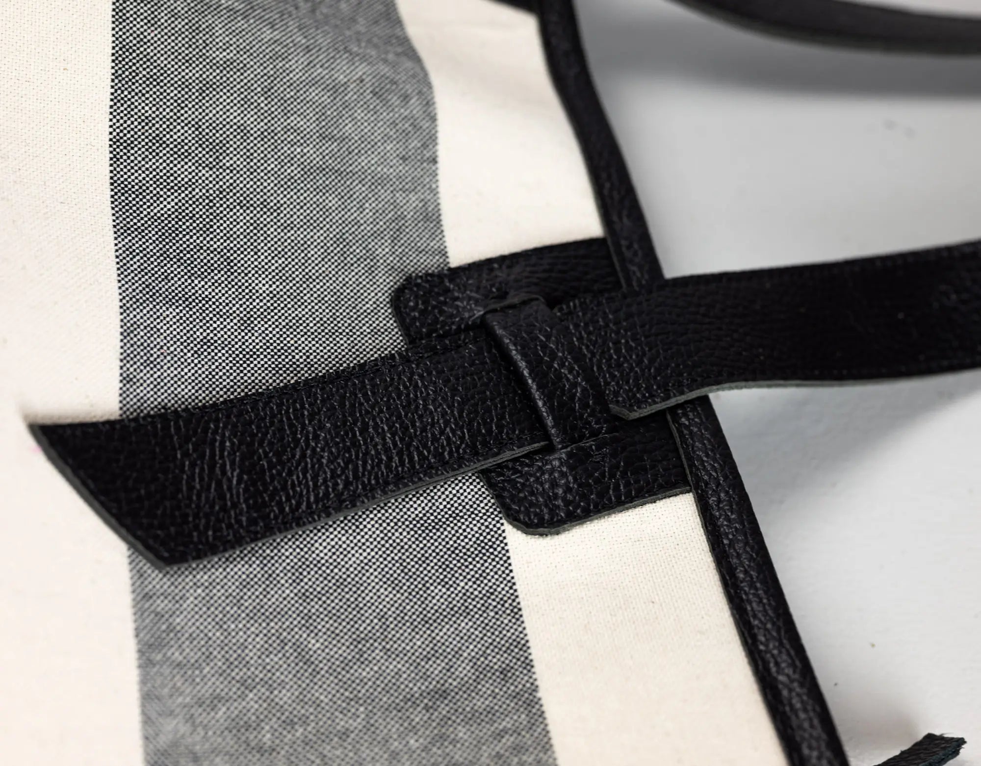 Close-up detail of a black pebbled leather strap crossing over a white and gray striped textile surface.