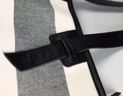 Close-up detail of a black pebbled leather strap crossing over a white and gray striped textile surface.