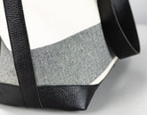 Close-up of a structured handbag corner showing black pebbled leather trim and strap against a white and gray woven fabric body.