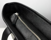 Close-up of the interior of a black pebbled leather bag, showing a silver zipper and a small matching leather pull tab against a light gray background.