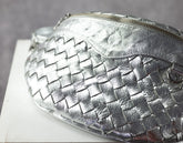 Silver woven handbag on a white surface with a gray background