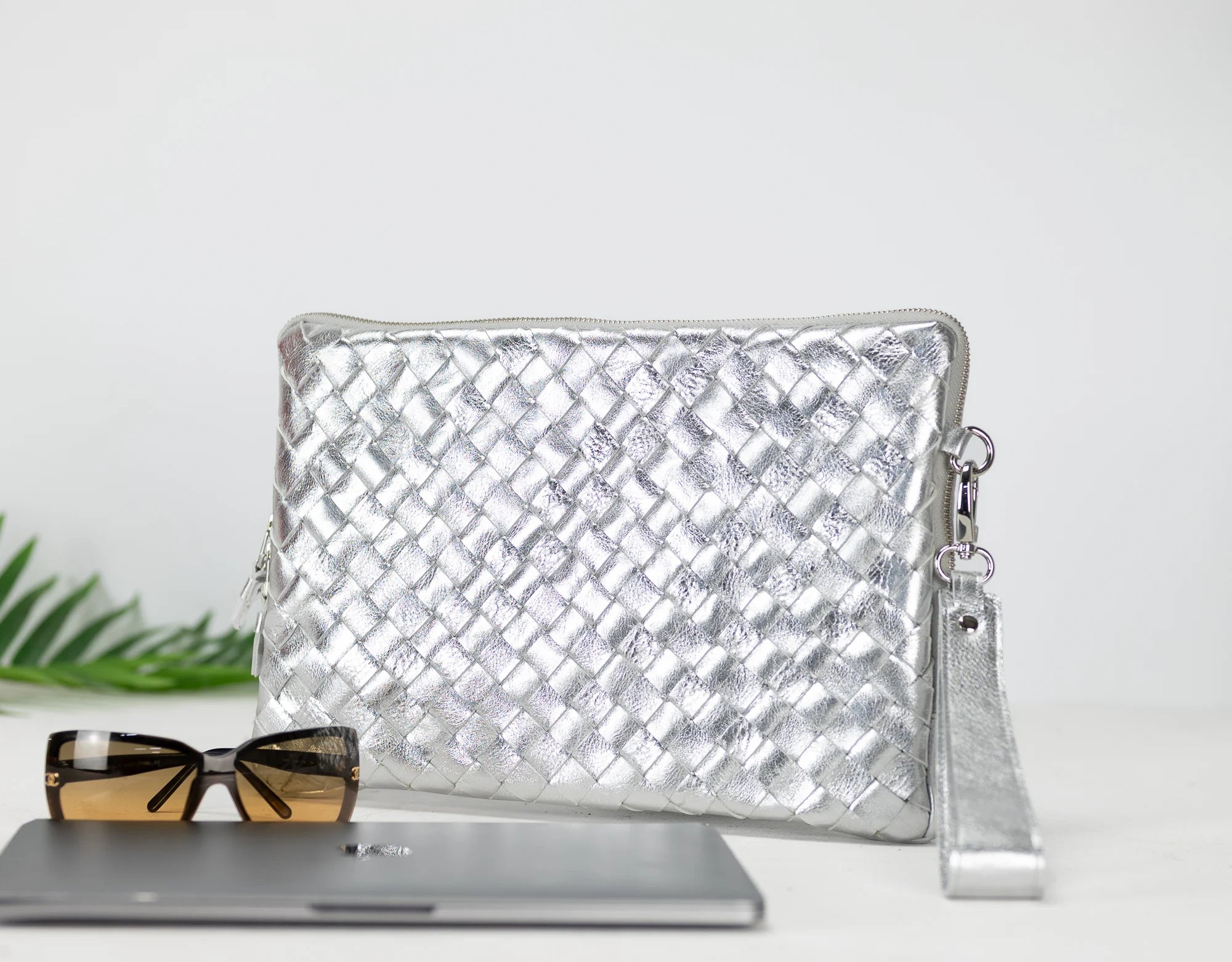 Silver woven clutch bag with sunglasses on a white surface