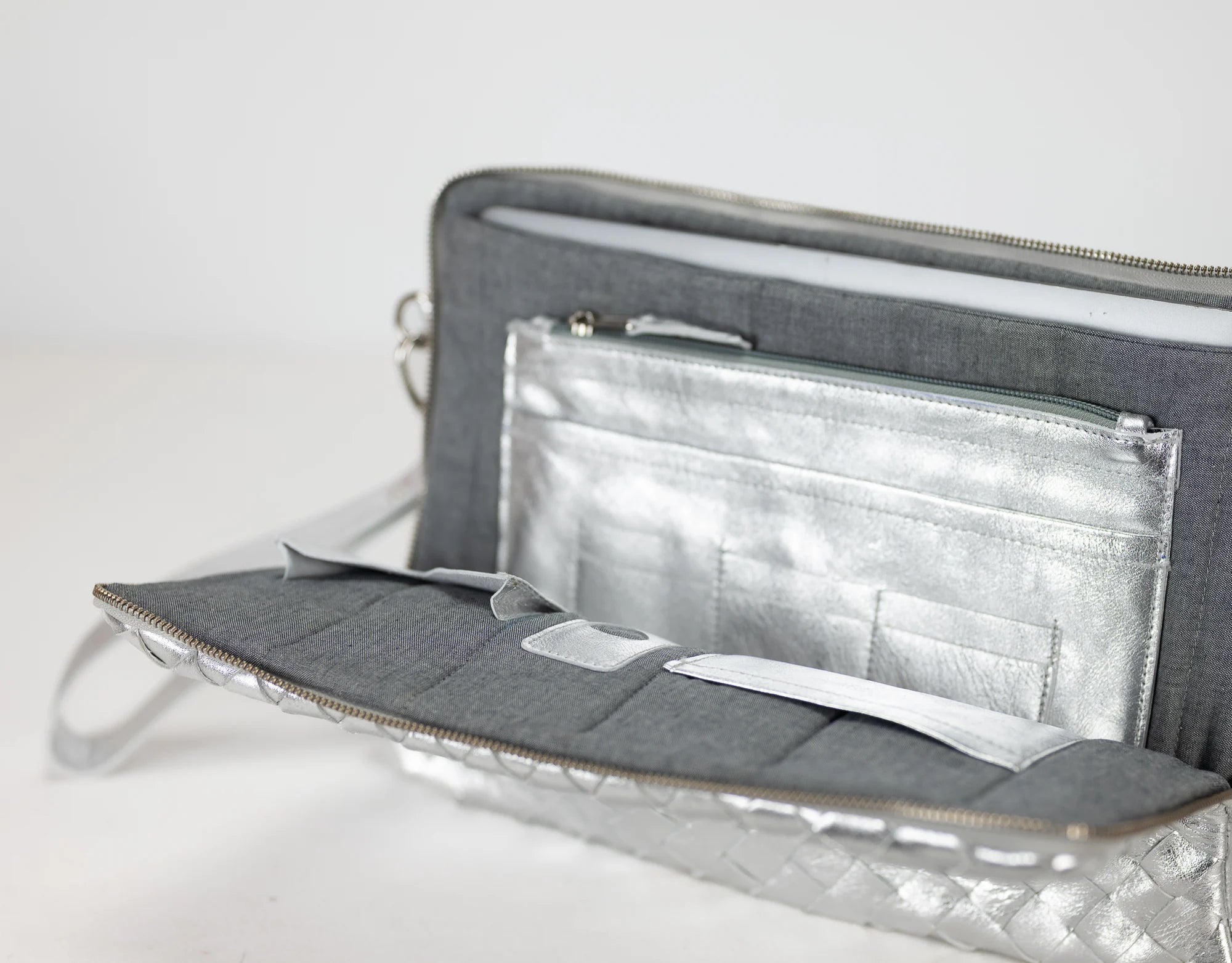 Gray clutch bag with open interior showing compartments on a light gray background