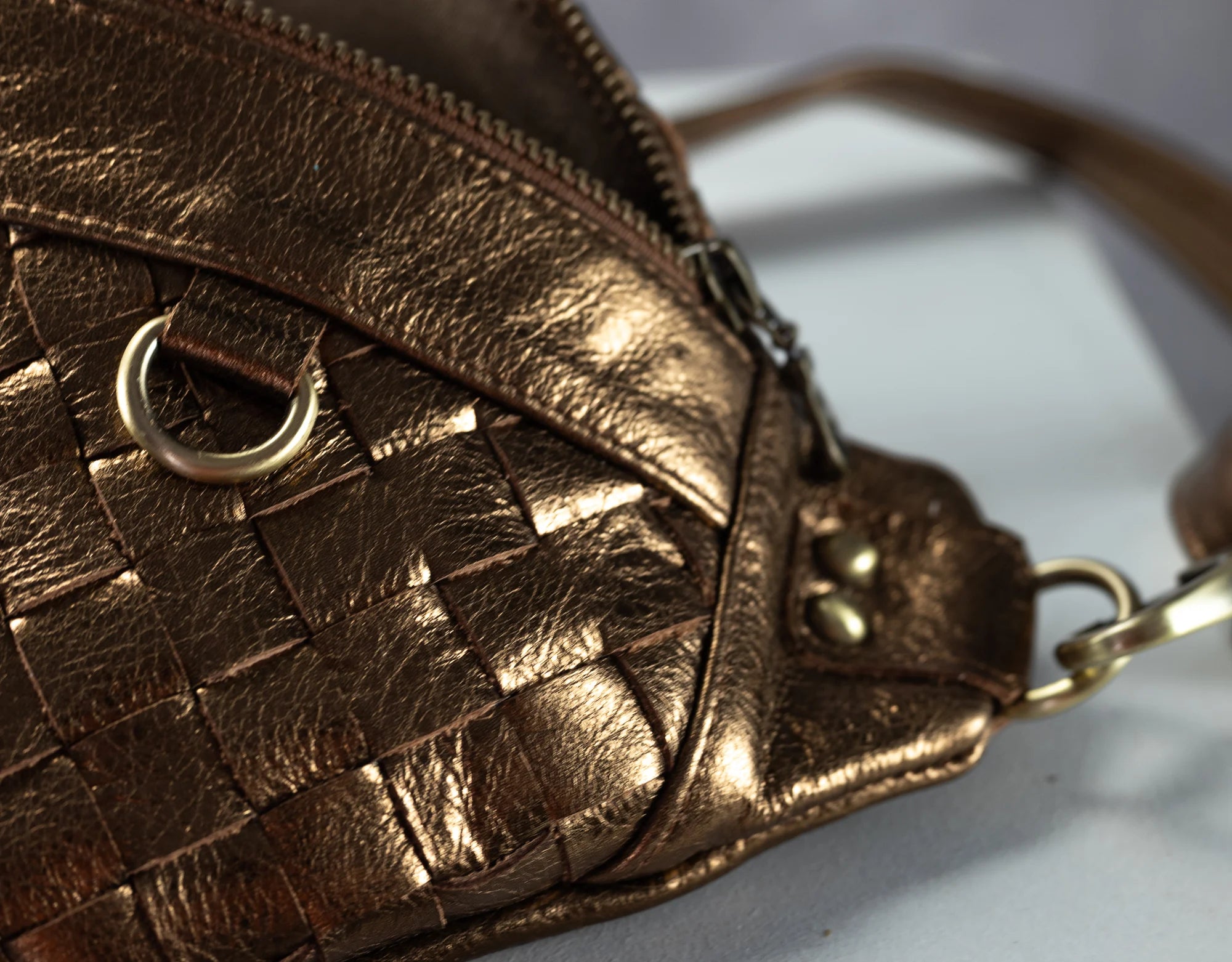 Close-up of a bronze woven handbag with a strap on a light background