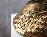 Brass woven handbag on a gray background