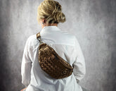 Person wearing a textured brass bag over their shoulder against a gray background