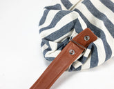 Blue and white striped bag with a brown leather strap on a light gray background