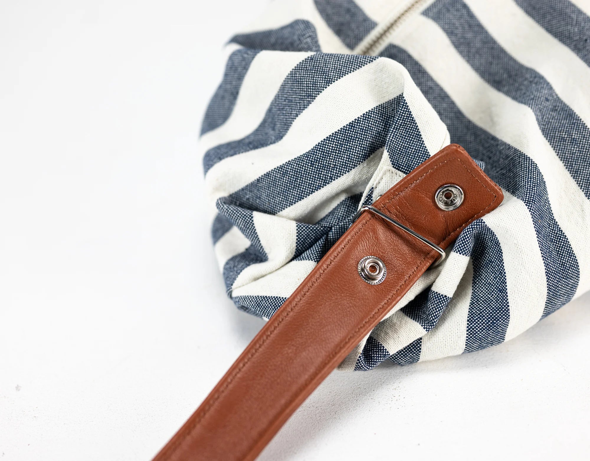 Blue and white striped bag with a brown leather strap on a light gray background
