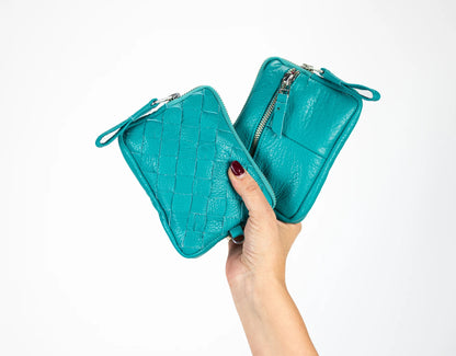 Turquoise leather clutch held by a hand on a white background