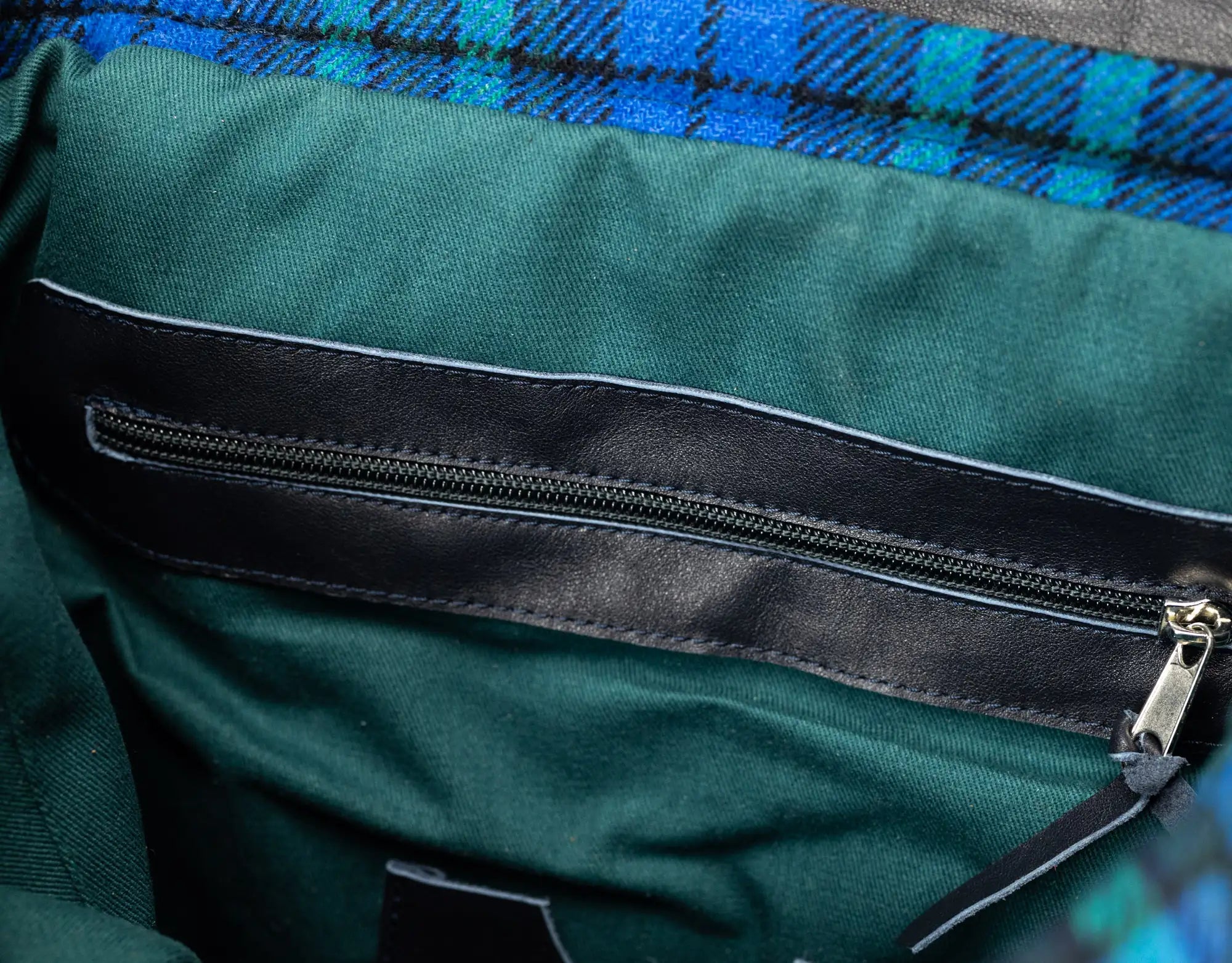 Close-up of a green fabric with a black zipper and plaid pattern in the background