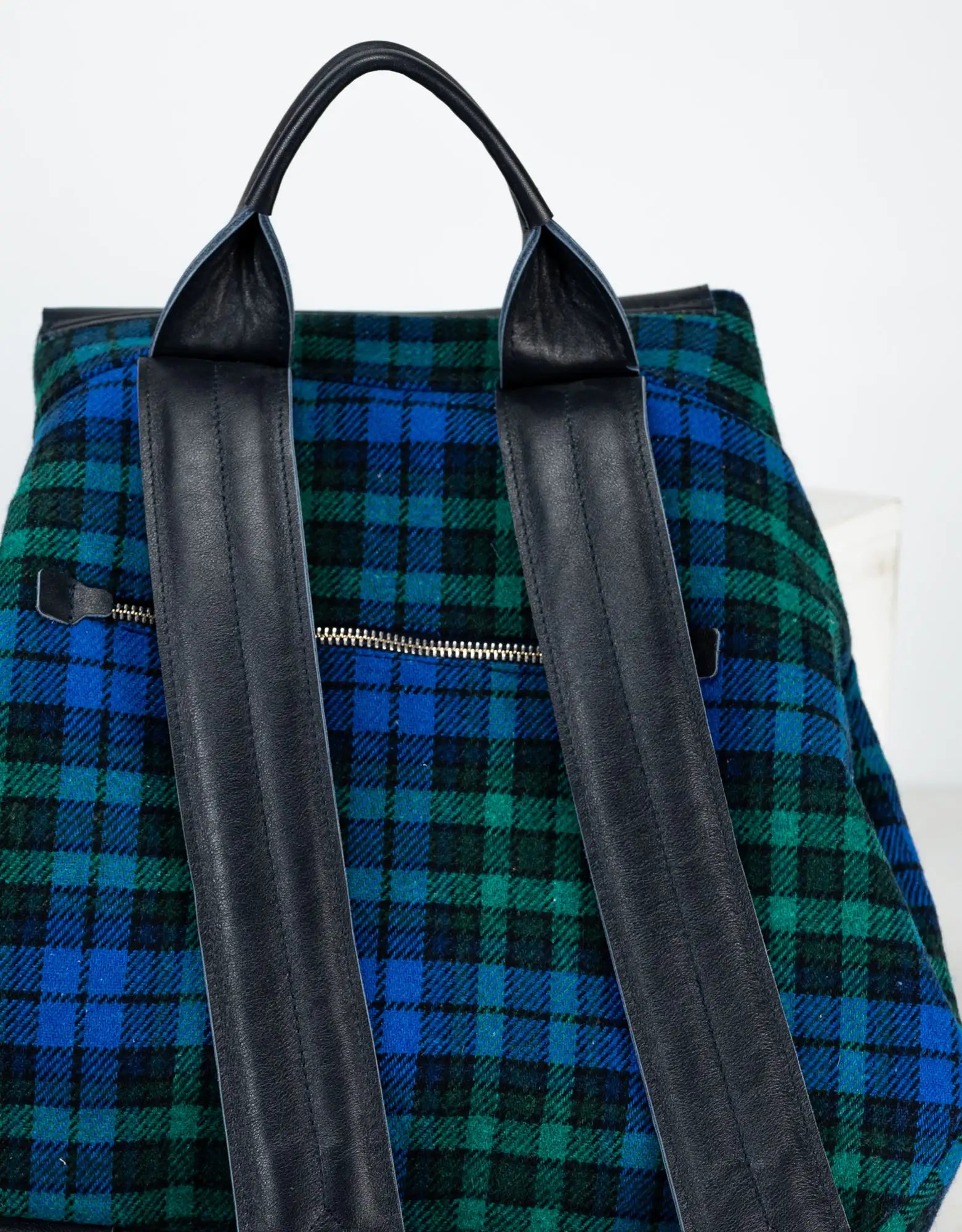 Green and blue plaid backpack with black straps on a white background