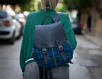 Person wearing a green sweater and plaid backpack on a street with blurred background