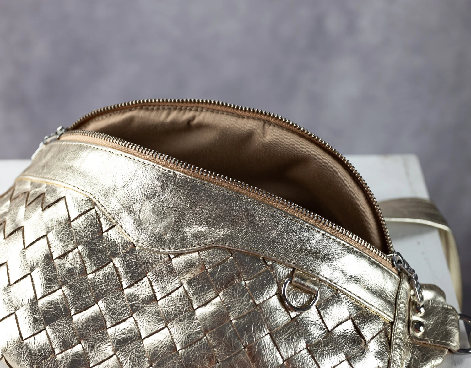 yellow gold woven handbag with a zipper on a gray background
