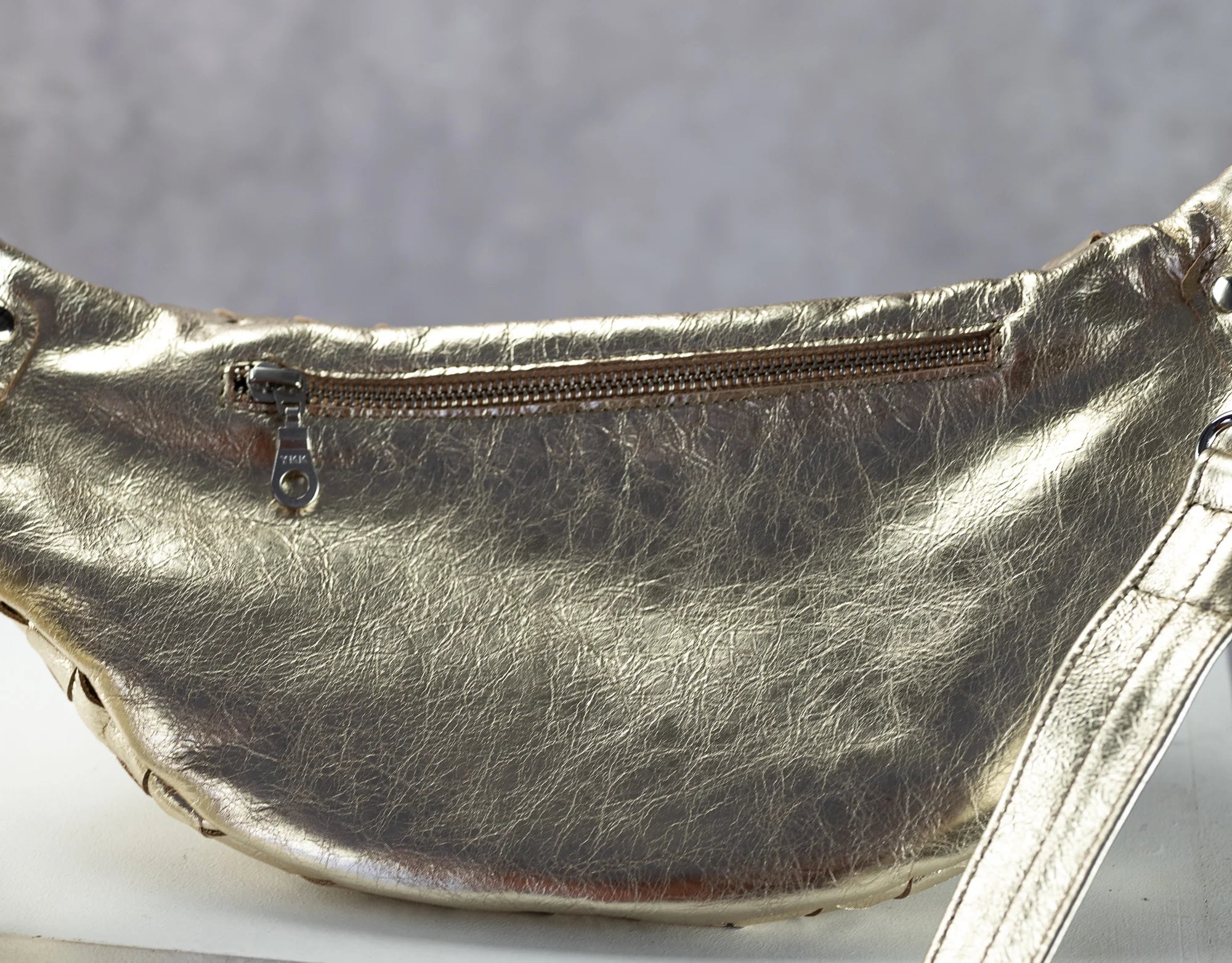 Metallic yellow gold fanny pack with a zipper on a gray background