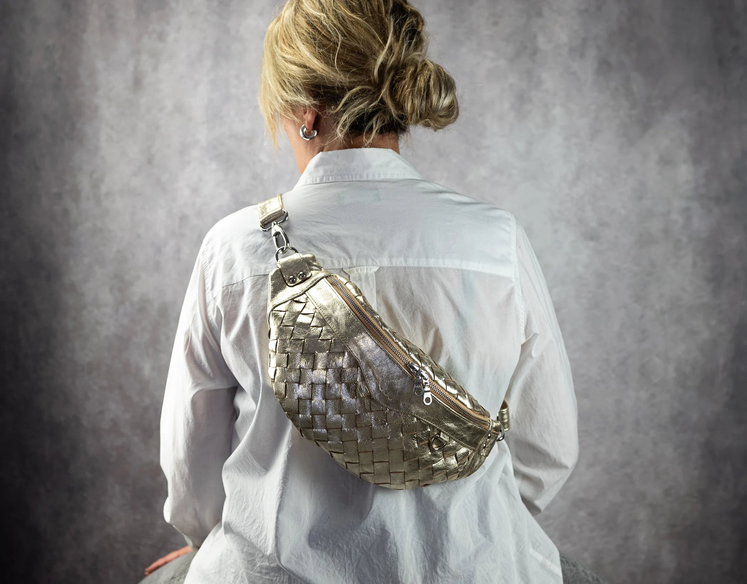 Person wearing a woven yellow gold bag over their shoulder against a gray background