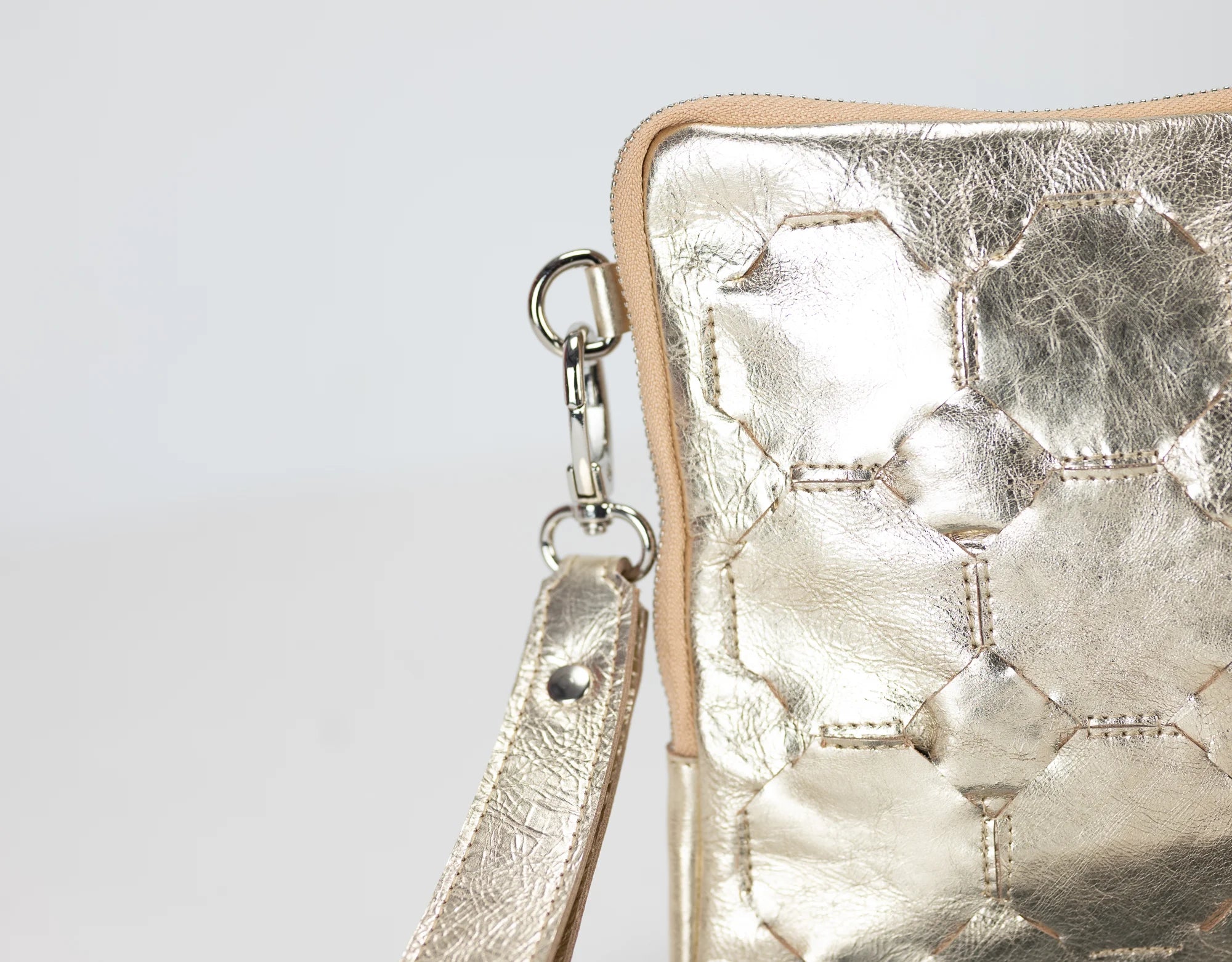 Metallic gold handbag with a strap on a light gray background