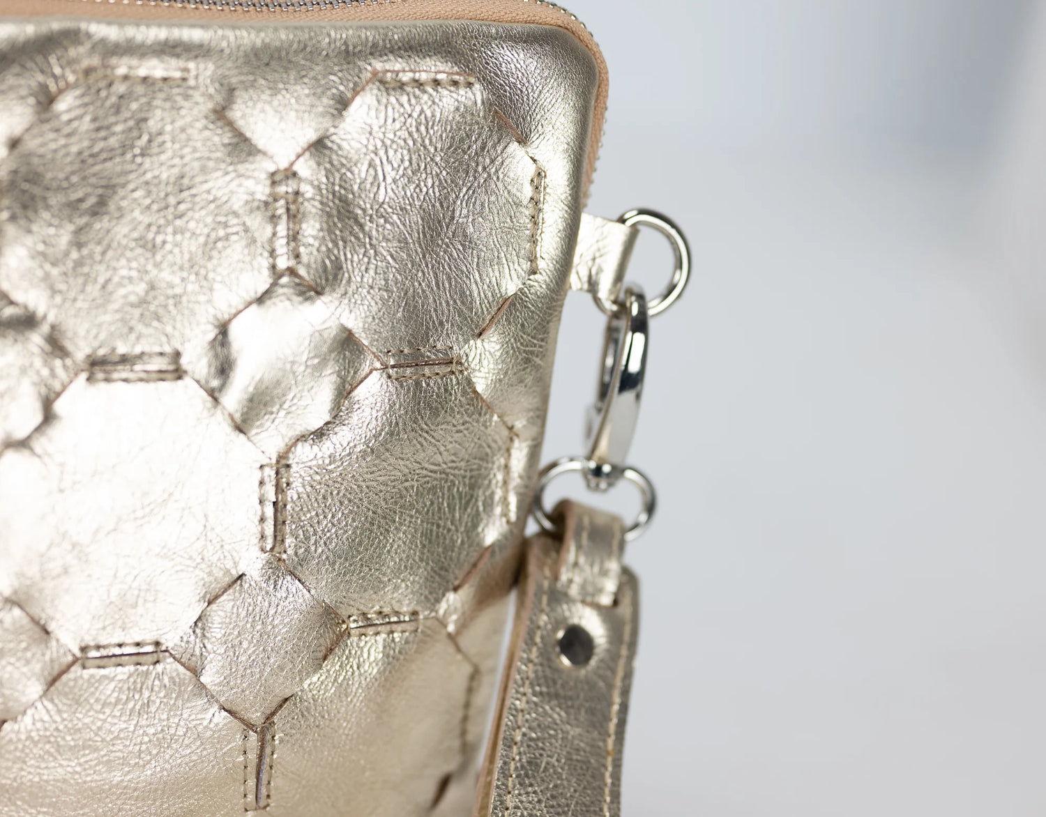 Close-up of a gold textured handbag with a keychain on a light gray background