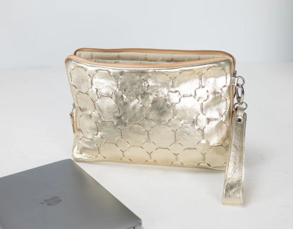 Gold textured clutch bag on a white surface with a laptop