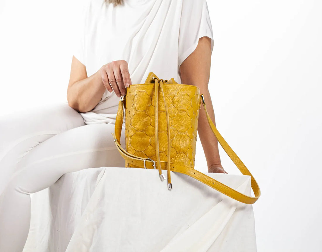 Yellow quilted handbag held by a person wearing a white outfit on a light background