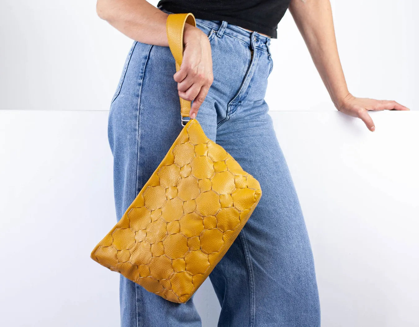 Person holding a mustard yellow woven clutch bag against a white background