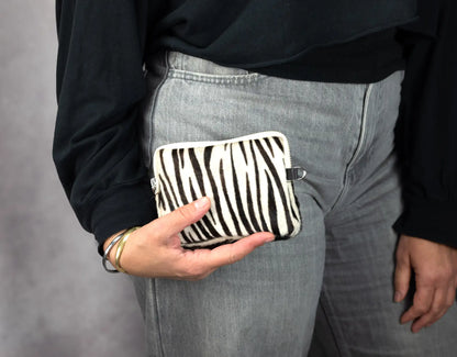Person holding a zebra-striped pouch against a gray background