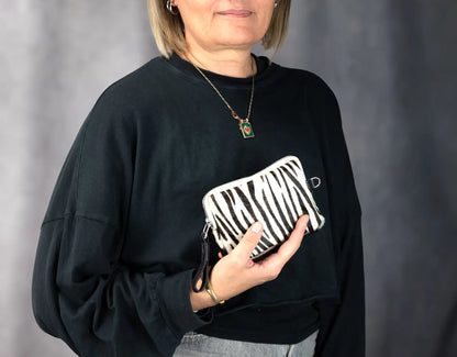 Person wearing a black sweatshirt holding a zebra-striped clutch against a gray background