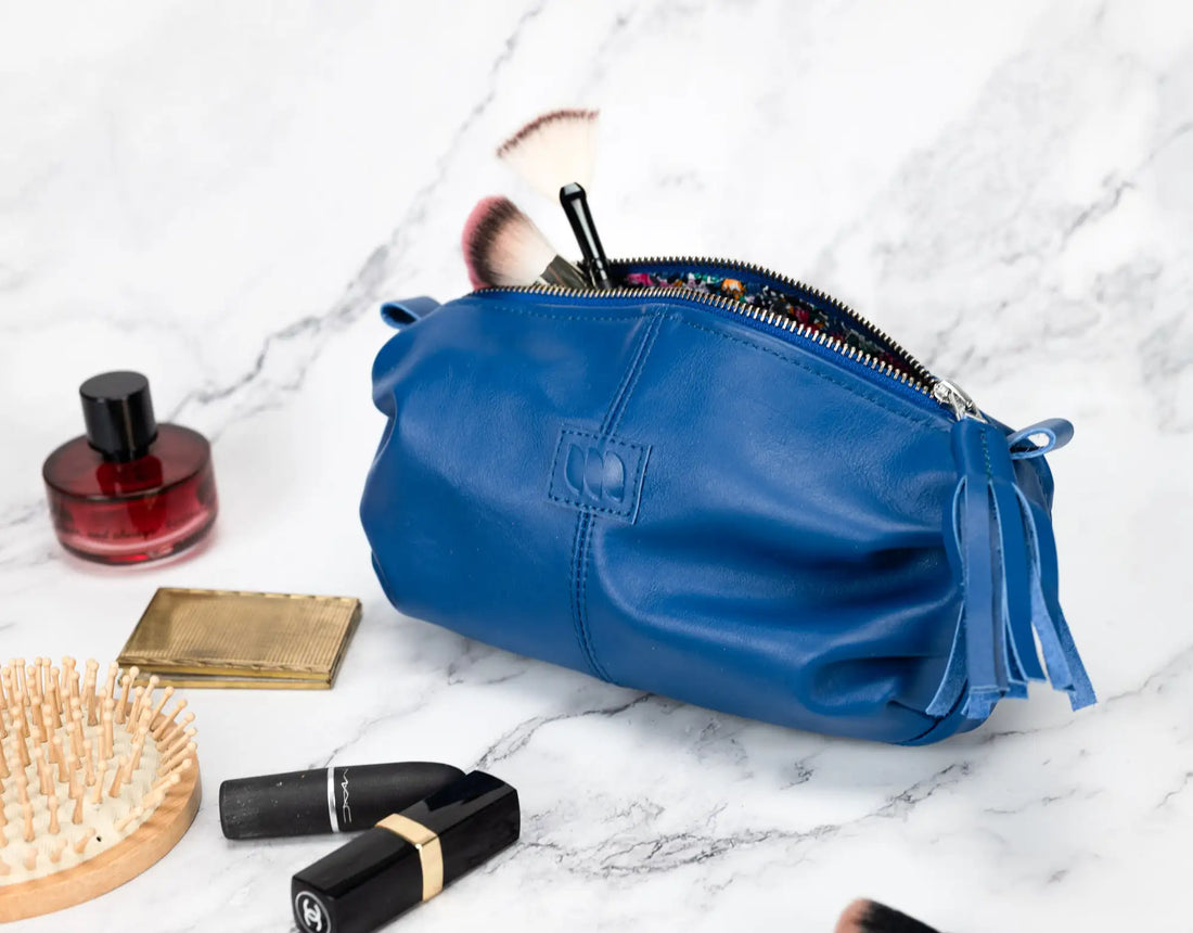 Blue makeup bag with cosmetic items on a marble surface