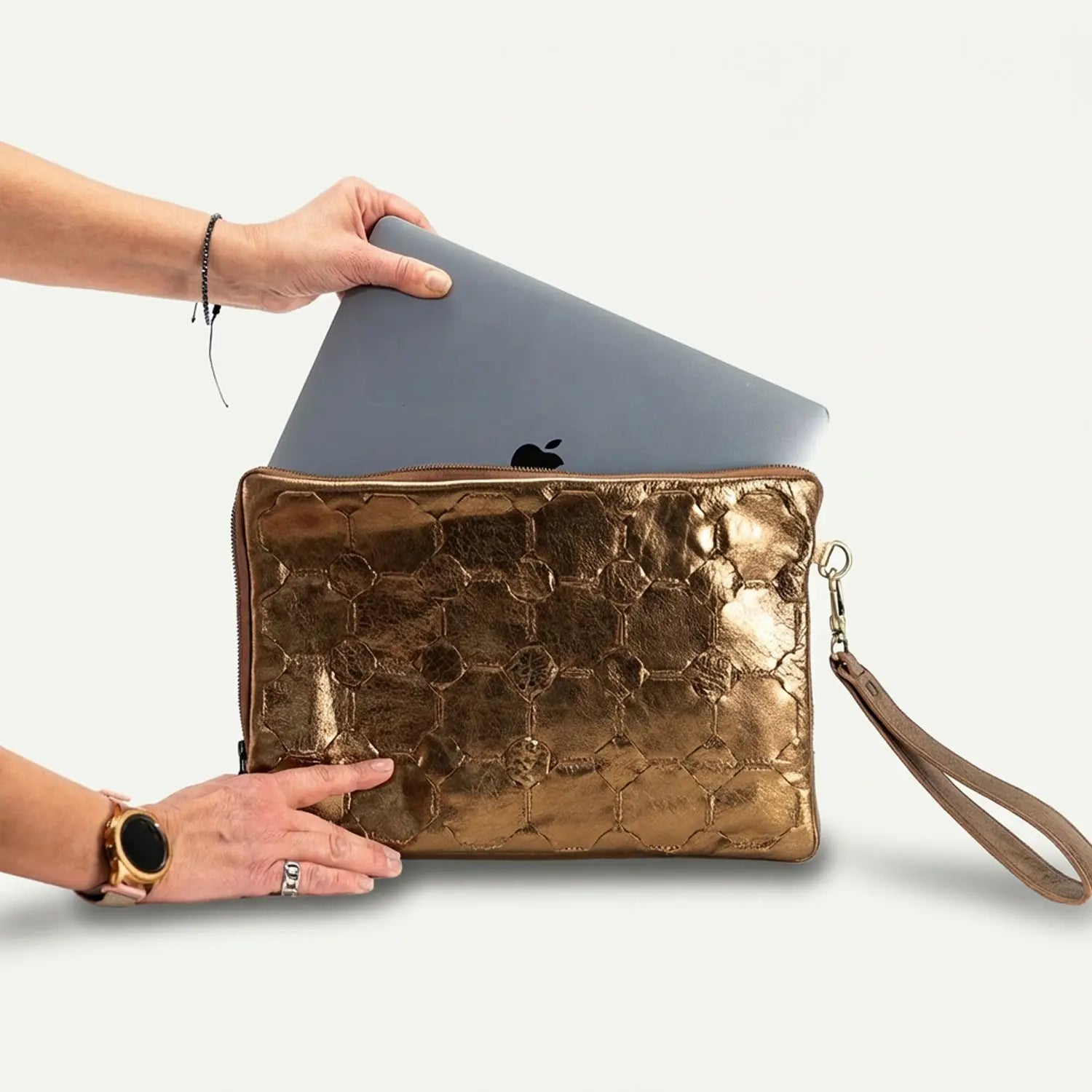 Gold clutch with a laptop being placed inside on a white background