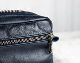 Close-up of a navy blue leather bag with a gold zipper on a light background