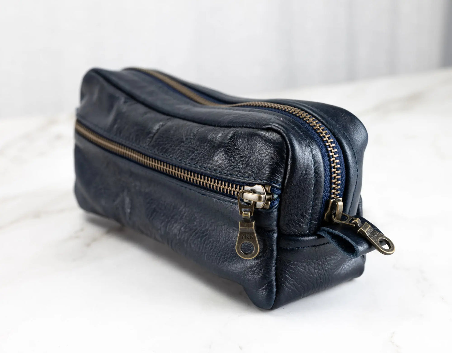 Blue leather pouch with gold zippers on a white surface