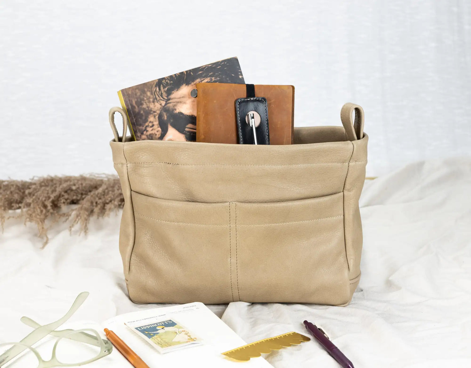 Beige fabric basket with books and stationery items on a white surface
